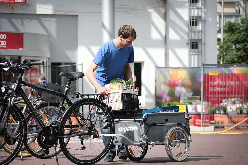 Anhänger Ein Mann belädt einen Fahrradanhänger vorm Supermarkt.